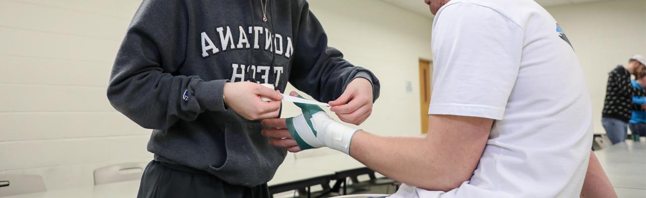 Student taping someone's hand with pre-wrap and tape